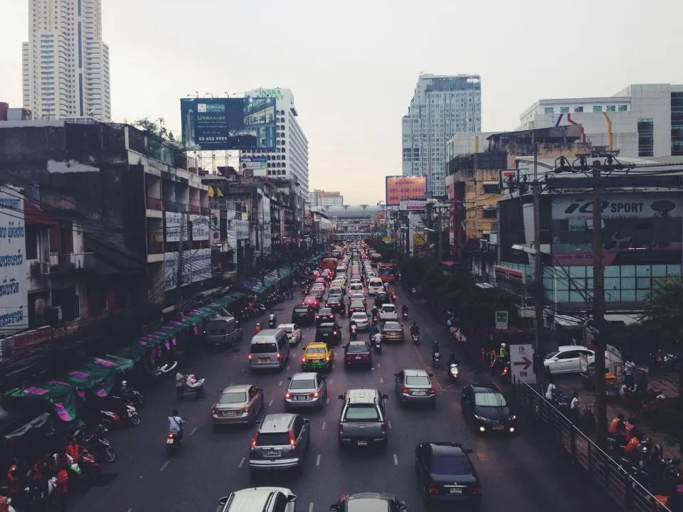 Busy Bangkok avenue with cars and motorbikes between high-rise buildings